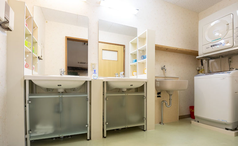 介護施設の洗面・浴室設備。二つの洗面台と乾燥機、オムツ用ゴミ箱が配置されている